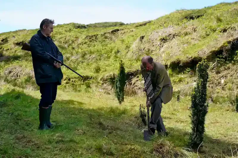 finbar mit gewehr und ein mann mit schaufel auf einer lichtung