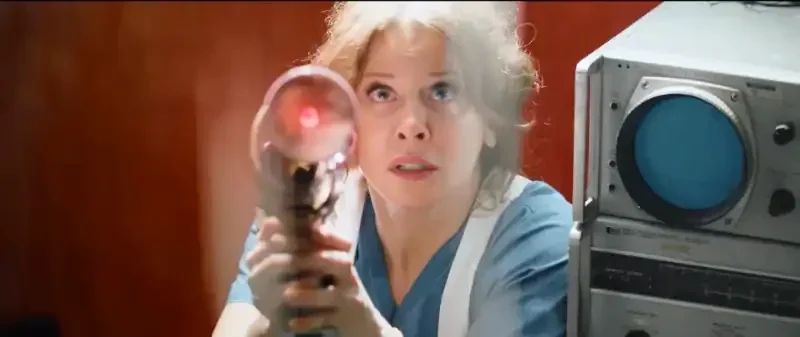 Cyst - Filmszene: Frau zielt mit futuristischer Waffe, technisch ausgestatteter Raum.