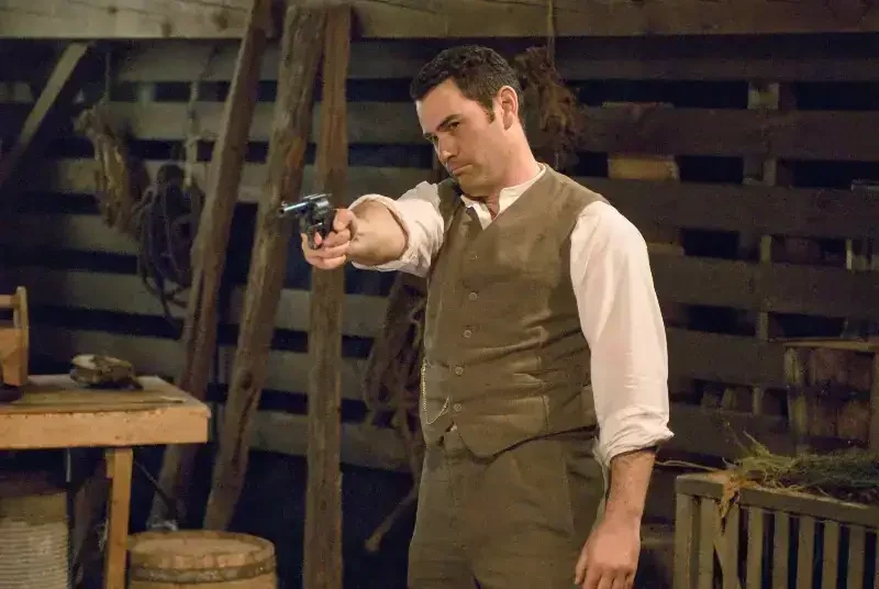Murdoch Mysteries Staffel 1 Szenenbild: Mann zielt mit Pistole in Scheune.