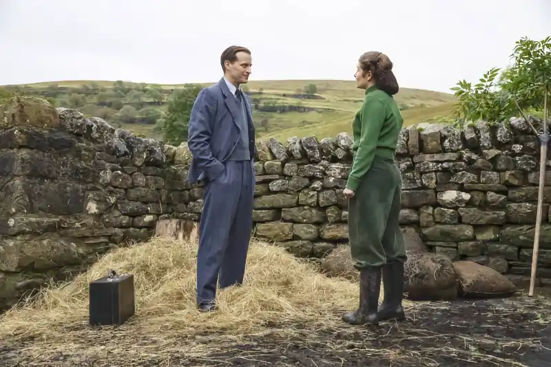Der Doktor und das liebe Vieh Staffel 1 Szene: Zwei Personen sprechen vor einer Steinmauer auf dem Land.