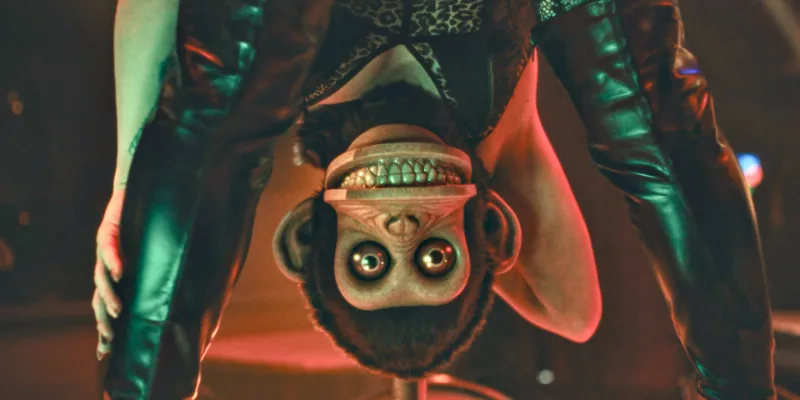 The Monkey Filmszene: eine Frau mit Affenkopf schaut durch ihre Beine