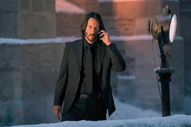 Schauspieler Keanu Reeves als John Wick auf einem schneebedeckten Balkon einer Kirche mit Handy in der Hand