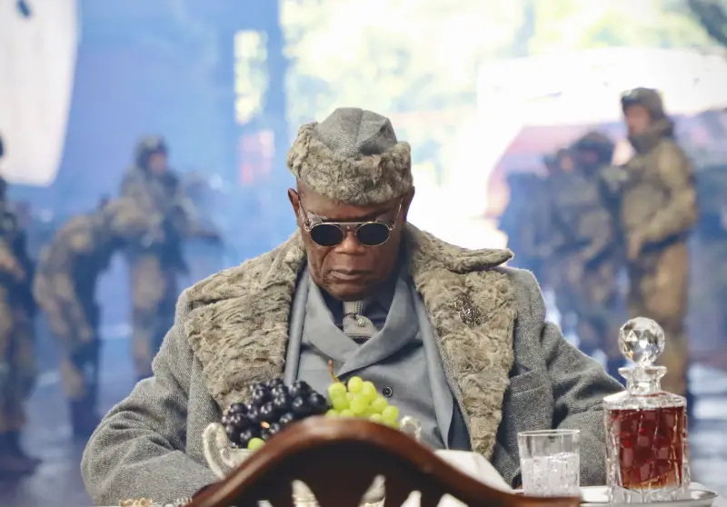 Darsteller Samuel L. Jackson mit Mantel und Fellmütze sitzend vor einem Tisch mit Trauben und Cognac Karaffe - Afterburn Filmszene