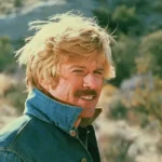 Darsteller Robert Redford mit hochgeschlagenen Hemdkragen und Schnurrbart in einer grünen Steppenlandschaft