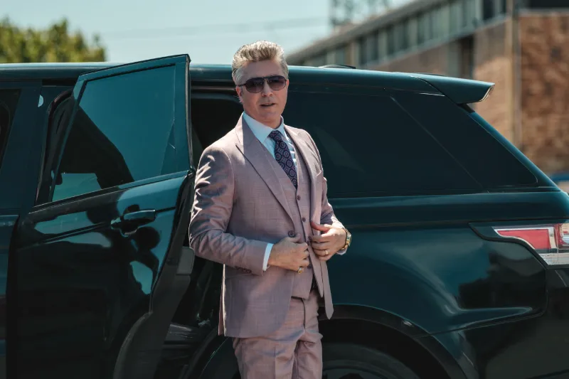 Darsteller Aiden Gillen im Anzug vor einem schwarzen SUV in Filmszene aus London Calling