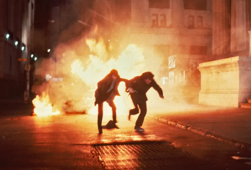 Zwei Personen, die vor einer großen Explosion hinter ihnen flüchten - Filmszene aus Wolfen