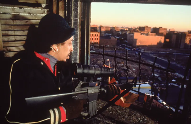 Ein Mann (Darsteller Gregory Hines) mit Funkgerät im Ohr und einem Scharfschützengewehr an einem Fenster - Filmszene aus Wolfen