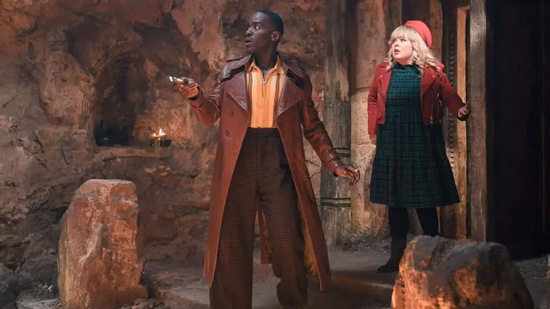 Ein Mann im Ledermantel und eine Frau mit roter Mütze in einer Höhle - Szene aus Dr. Who Joy of the World