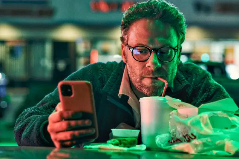Seth Rogen vor seinem Handy mit Strohhalm im Mund - nächtliche Szene am Auto - Good Fortune