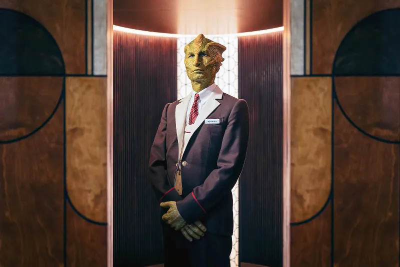 Ein außeriridisches Echsenwesen, im Anzug mit Namensschild - Szene Dr. Who Joy of the World