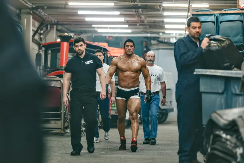 Filmszene aus The Smashing Machine: Dwayne Johnson läuft als UFC Kämpfer mit nacktem, muskulösem Oberkörper durch einen Backstagebereich.