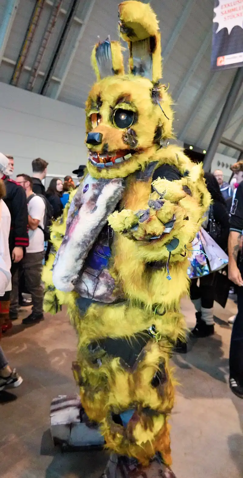 Ein Mann verkleidet als gelber Zombie Roboter Bär, der seine Hand ausstreckt