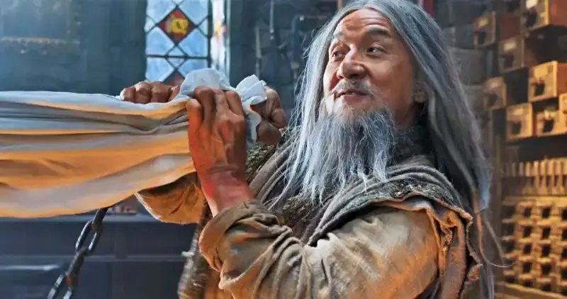 Ein älterer Mann (Jackie Chan) mit langen, grauen Haaren wehrt einen Faustschlag ab - Szene aus Iron Mask