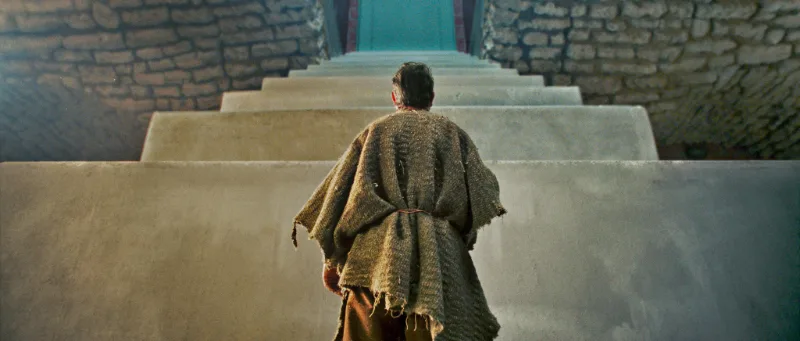 Der geschrumpfte Paul (Jean Dujardin) gekleidet in Stofffetzen vor einer riesigen Kellertreppe- Filmszene - Der Mann der immer kleiner wurde