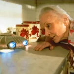 Eine Frau (Darstellerin Jessica Tandy) beugt sich auf ihrem Küchentresen zu einem kleine UFO hinunter - Filmszene