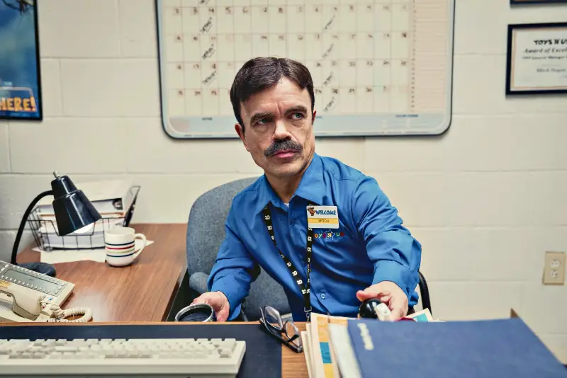 Mann (Schauspieler Peter Dinklage) im Büro mit Namensschild und Stempel - Filmszene
