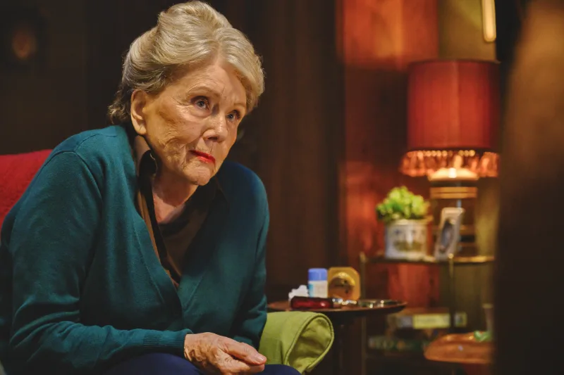 Ältere Frau (Schauspielerin Diana Rigg) sitzt nachdenklich im Wohnzimmer - Filmszene