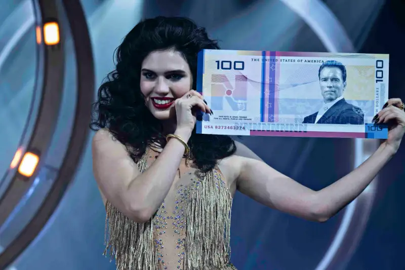 Frau hält übergroßen 100-Dollar-Geldschein auf Bühne - Filmszene The Running Man 2025