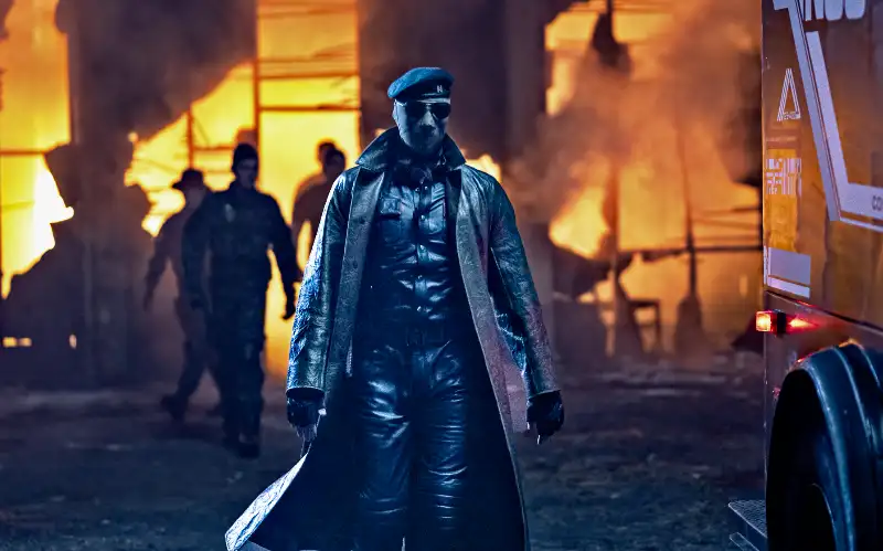 Person in Ledermantel vor brennendem Gebäude bei Nacht - Filmszene The Running Man 2025