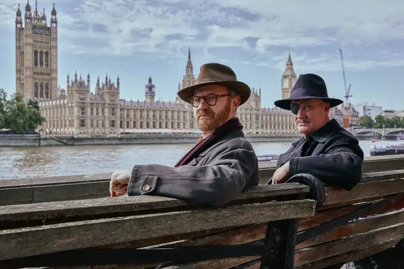 Zwei Männer mit Hüten auf Bank vor Westminster-Palast London