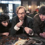 Drei Schauspieler liegen auf Teppich in düsterer Szene aus der TV-Serie Bookish