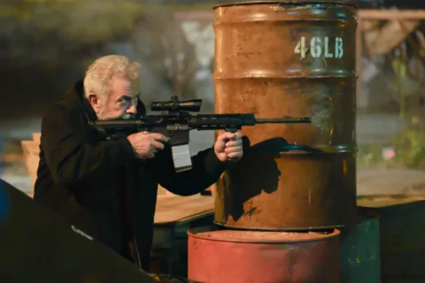 Mel Gibson als Bowdrie mit Sturmgewehr hinter Ölfässern in Hunting Season