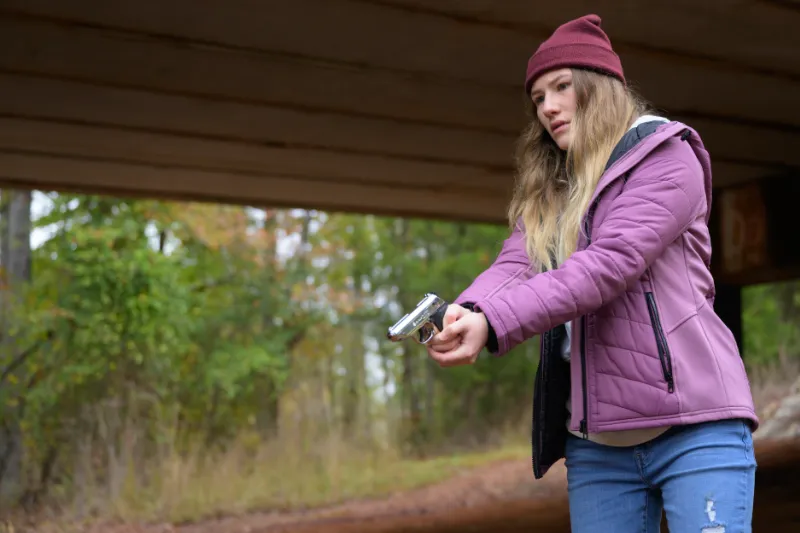 Sofia Hublitz als Tag steht mit Pistole unter einer Brücke - Szene aus Hunting Season