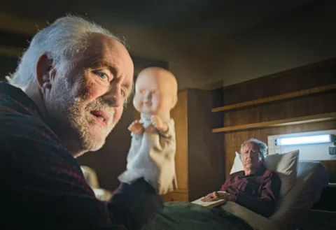 John Lithgow als Dave Crealy mit Handpuppe sitzt vor Geoffrey Rush - Szene aus The Rule of Jenny Pen