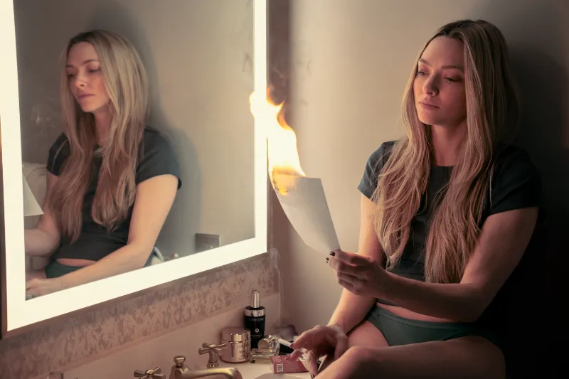 Darstellerin Amanda Seyfried sitzt vor einem Spiegel, in der Hand ein brennendes Bild aus The Housemaid