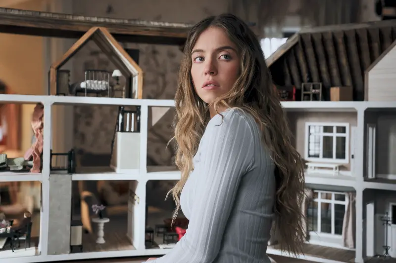 Sydney Sweeney als millie blickt überrascht zur Tür, vor ihr ein gruseliges Puppenhaus - Szene aus The Housemaid