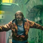 Mann in bunter Jacke steht dramatisch in grünem Korridor