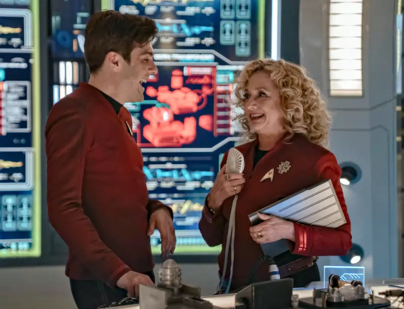 Zwei Schauspieler in Star-Trek-Uniformen lachen auf dem Maschinendeck eines Raumschiffs