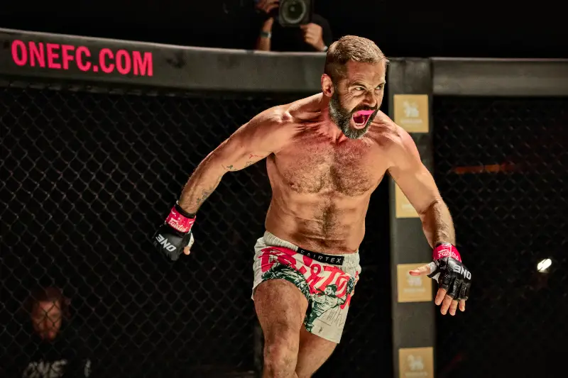 Ein muskulöser MMA-Kämpfer greift schreiend seinen Gegner im Käfig an.