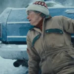 Frau in Winterjacke blickt alarmiert hinter blaues Auto im Schnee.