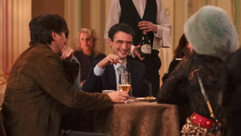 Lachender Mann mit Zigarette an einem Tisch, mit einem Mann und einer Frau im Restaurant.