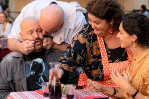 Schauspieler Kevin James als Matt mit drei Personen an einem Tisch mit Rotwein - Filmszene aus Solo Mio