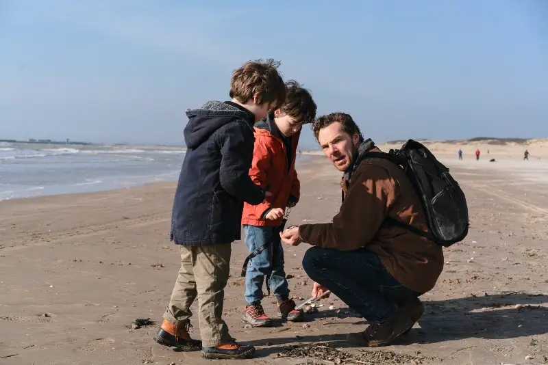 Benedict Cumberbatch kniet mit zwei Kindern am Sandstrand und sucht nach Muscheln