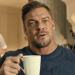 Alan Ritchson hält eine weiße Kaffeetasse und blickt aufmerksam nach vorne