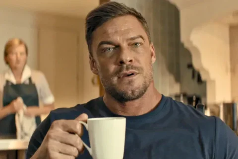Alan Ritchson hält eine weiße Kaffeetasse und blickt aufmerksam nach vorne