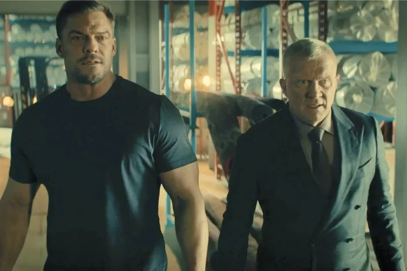 Alan Ritchson als Jack Reacher und Anthony Michael Hall gehen aufmerksam durch eine Lagerhalle