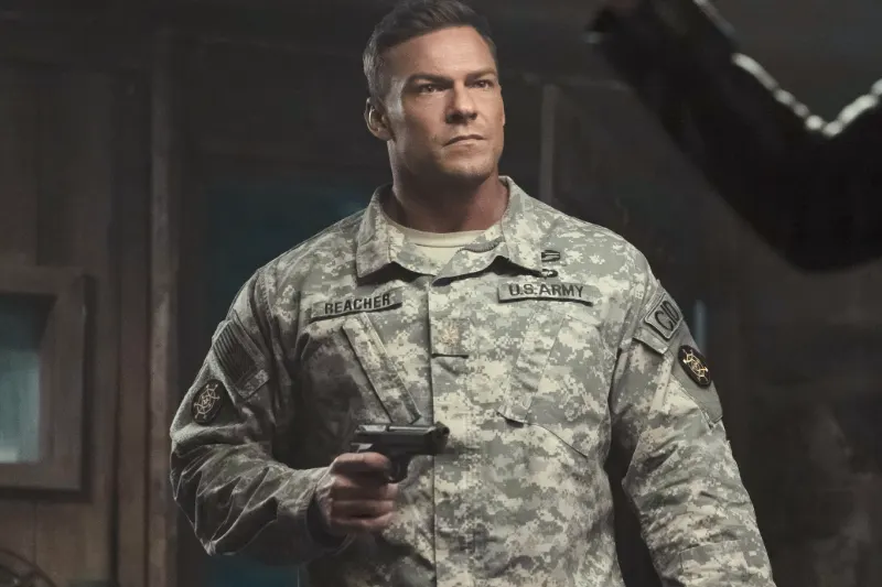 Alan Ritchson als Jack Reacher in U.S.-Army-Tarnuniform mit einer Pistole in der Hand