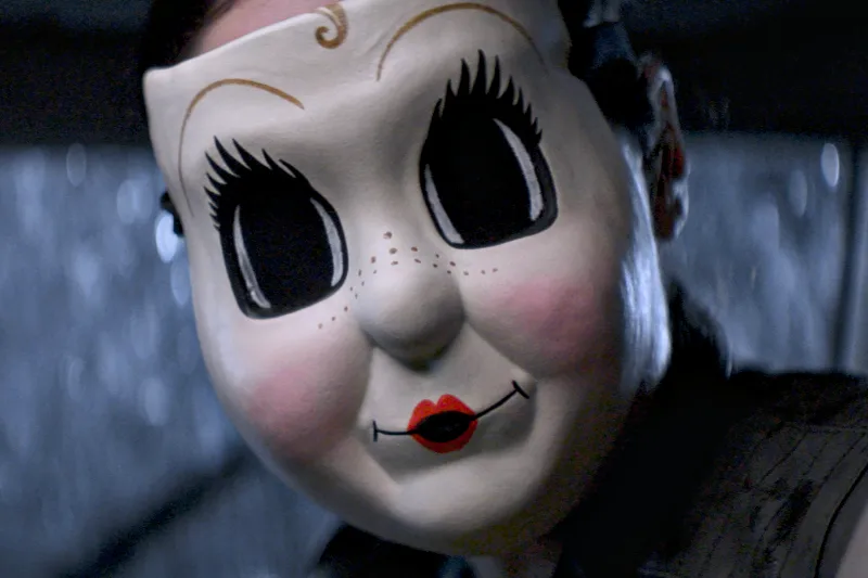 Nahaufnahme einer Person mit einer puppenähnlichen weißen Maske und übergroßen schwarzen Augen